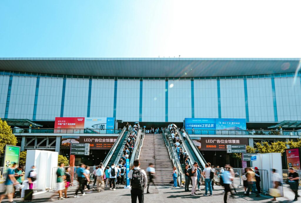 Feiras da China 2026 — entrada do National Exhibition and Convention Center (NECC) em Shanghai com visitantes B2B subindo escadas rolantes para feira internacional