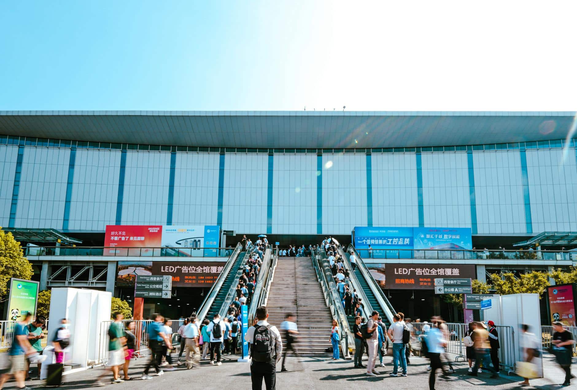 Feiras da China 2026 — entrada do National Exhibition and Convention Center (NECC) em Shanghai com visitantes B2B subindo escadas rolantes para feira internacional