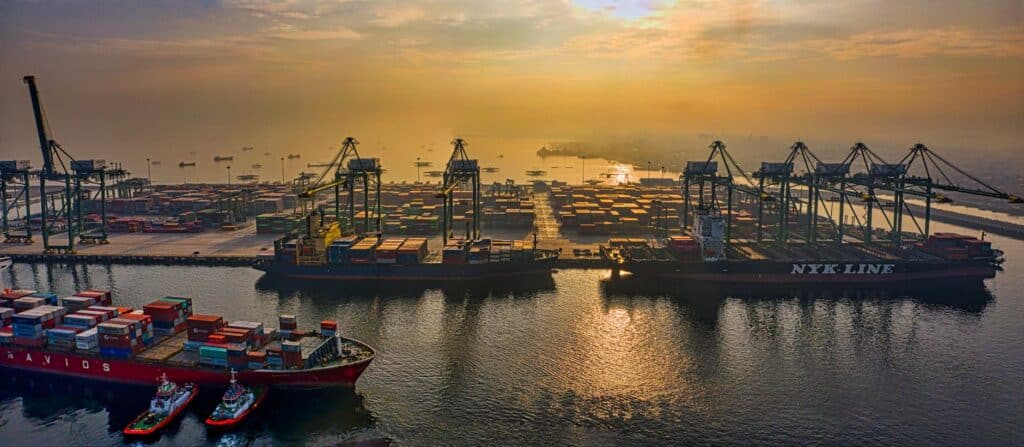Vista aérea de porto industrial brasileiro com guindastes e contêineres aguardando despacho aduaneiro