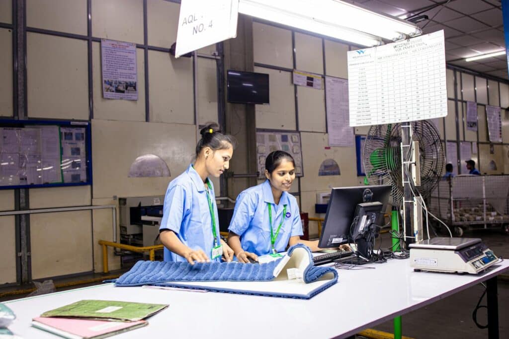Auditoria de fábrica na China: 2 inspetoras de qualidade em estação AQL conferindo produto têxtil em linha de produção asiática