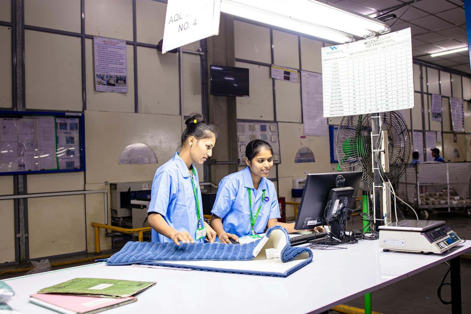 Auditoria de fábrica na China: 2 inspetoras de qualidade em estação AQL conferindo produto têxtil em linha de produção asiática